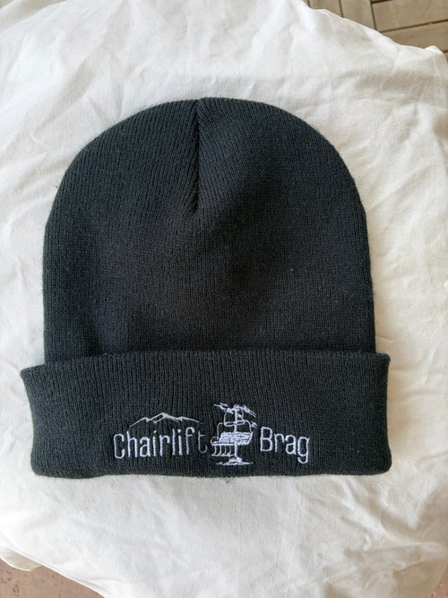 Black beanie with 'Chairlift Brag' embroidery on a white background