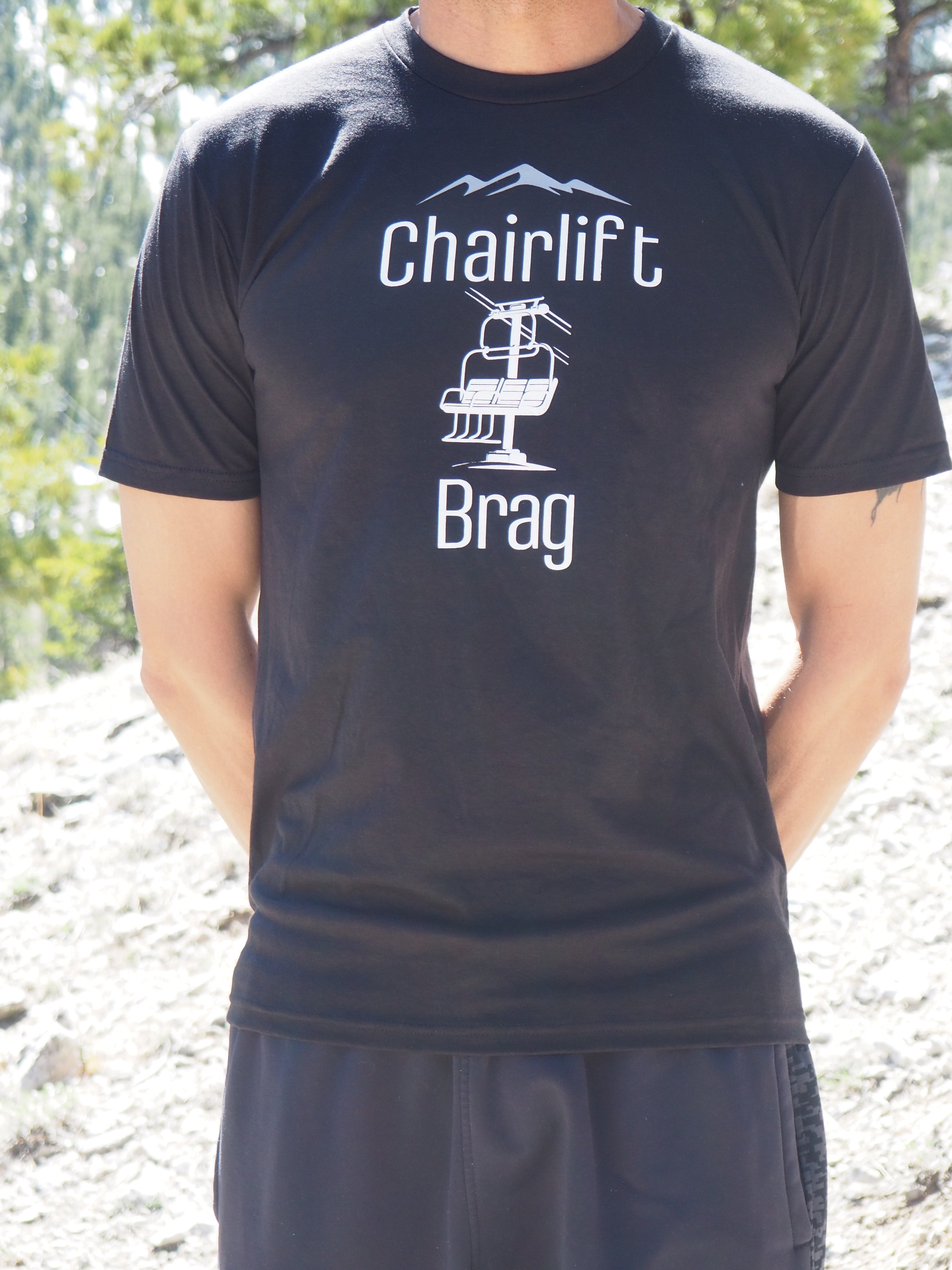 Person wearing a black t-shirt with 'Chairlift Brag' text and logo outdoors.